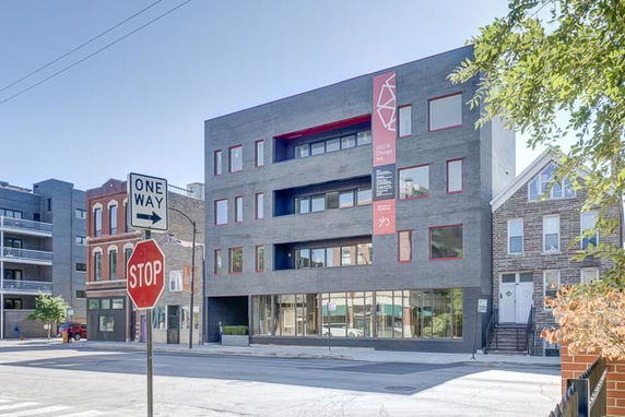 Front view of a modern four-story building with red accents and large windows.