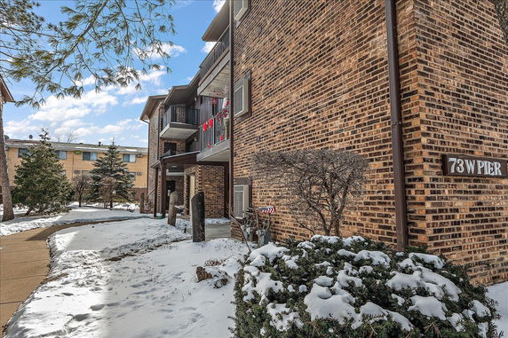 Front view of a brick apartment building with balconies and snow-covered ground.