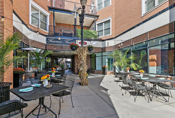 Outdoor seating area of a restaurant with tables and chairs on a sidewalk.