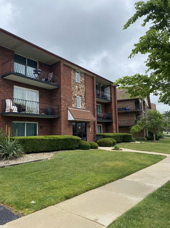 Front view of a three-story brick apartment building with balconies.