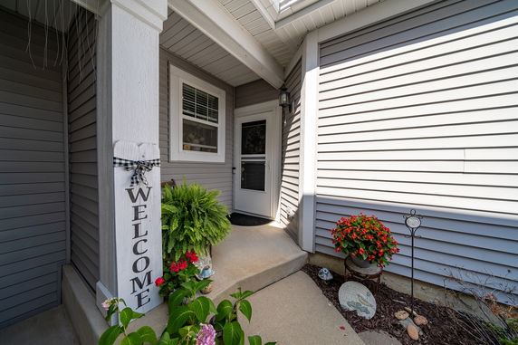 Front view of a house entrance with grey siding and a welcome sign.