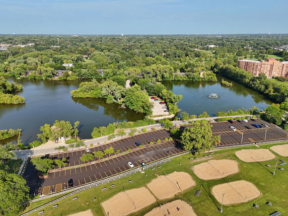 Aerial view of a large park area with a lake and parking lots, surrounded by trees and residential buildings.