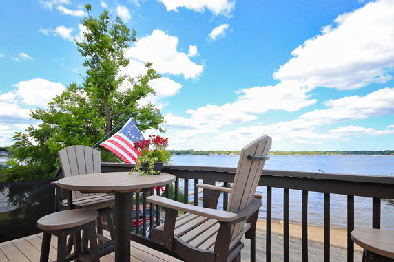 Deck view overlooking a lake with an American flag and outdoor seating.