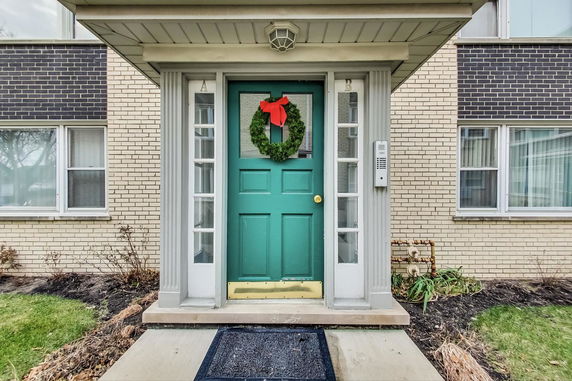 Front view of a building entrance with a teal door decorated with a wreath.