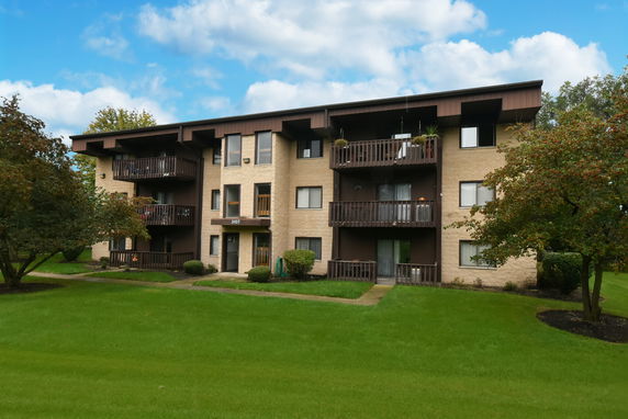 Front view of a three-story apartment building with balconies and a well-maintained lawn.