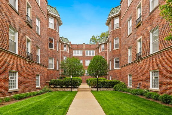 Front view of a brick residential apartment building with a walkway and lawn in the foreground.