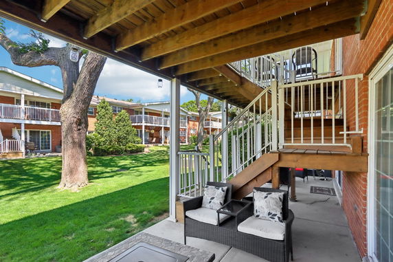 View of apartment buildings with balconies from a patio area, featuring a tree and grassy lawn.