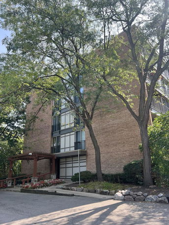 Front view of a multi-story brick apartment building with trees in front.