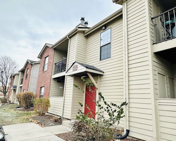 Front view of a multi-story residential building with balconies and a red door entrance.