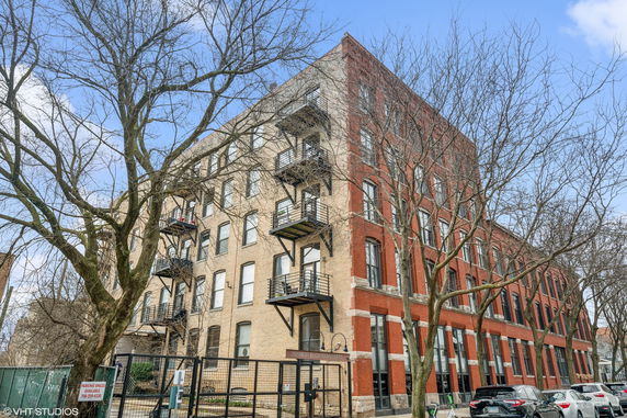 Front view of a multi-story brick apartment building with fire escape balconies.