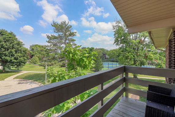 View of surrounding areas from a balcony showing trees and tennis courts.