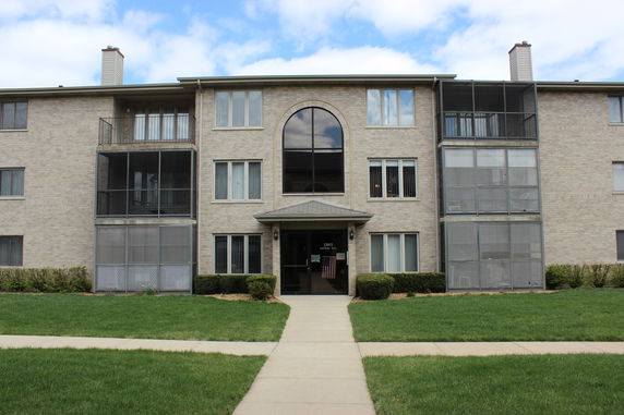 Front view of a multi-story apartment building with a central entrance and enclosed balconies.