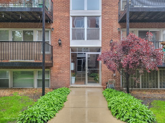 Front view of a brick apartment building with balconies and a glass entrance door.