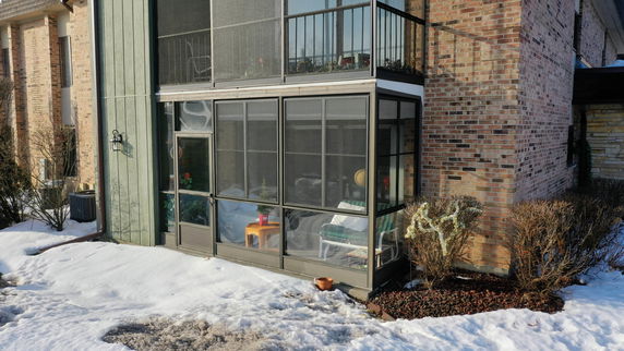 View of a brick residential building with a screened porch and glass enclosure.