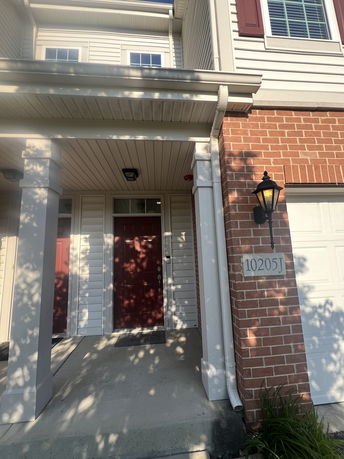 Front view of a house with brick and siding, featuring a covered entryway and a red door.
