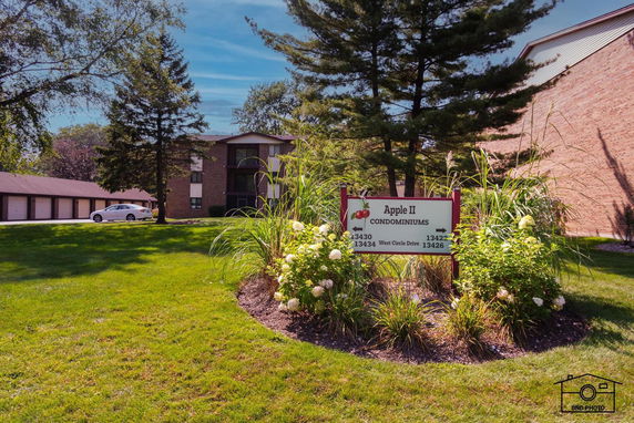 Front view of a condominium building with a sign and greenery.