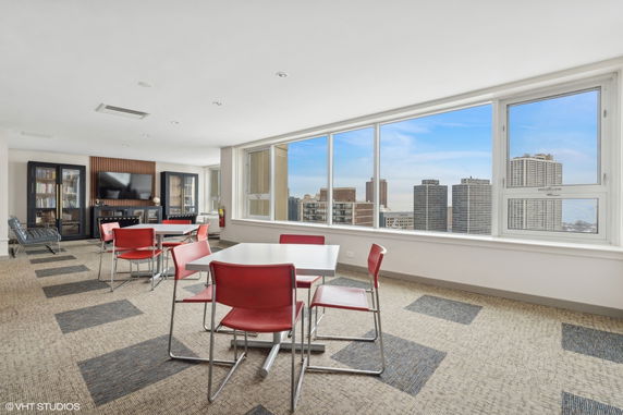 Indoor room with red chairs and tables, large windows with city view, and shelves.