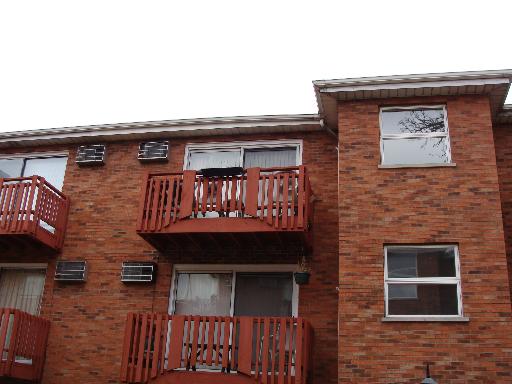 Front view of a multi-story building with red brick exterior and wooden balconies.