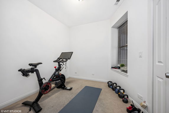 Room with exercise equipment including a stationary bike, yoga mat, and kettlebells.