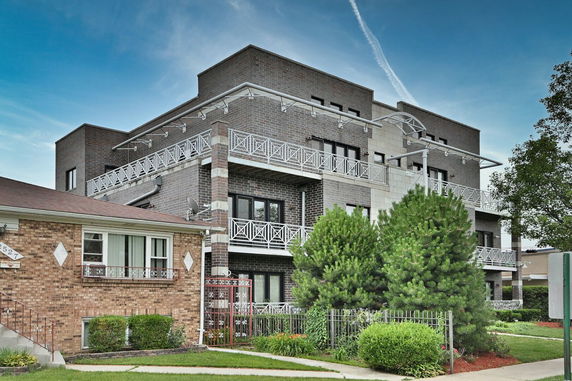 Front view of a multi-story brick building with balconies and decorative metal railings.
