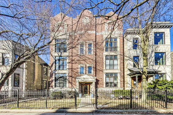 Front view of a multi-story brick building with large windows and a gated entrance.