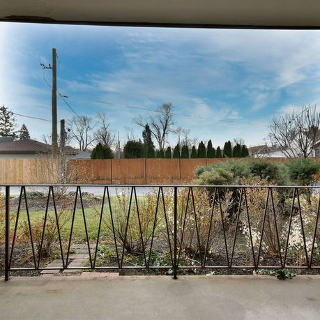 View from a porch overlooking a grassy yard and a wooden fence, with houses and trees in the background.