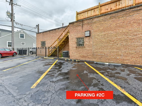 Outdoor parking area adjacent to a brick building with marked parking spaces and a visible staircase.