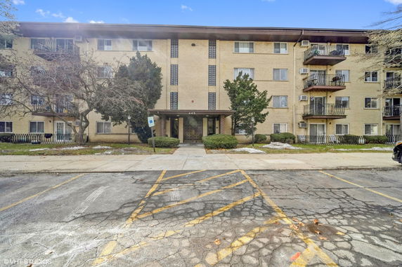 Front view of a multi-story residential building with balconies and entrance canopy.