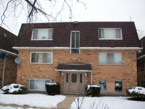 Front view of a two-story brick building with a sloped roof and large windows.
