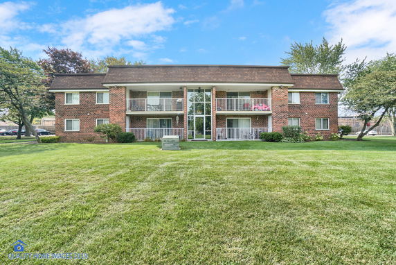 Front view of a two-story brick apartment building with balconies and a lawn.