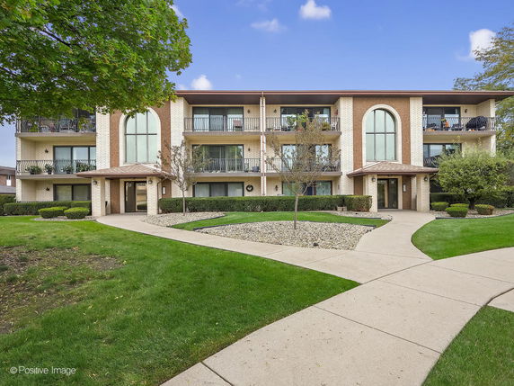 Front view of a three-story apartment building with balconies and landscaped pathways.