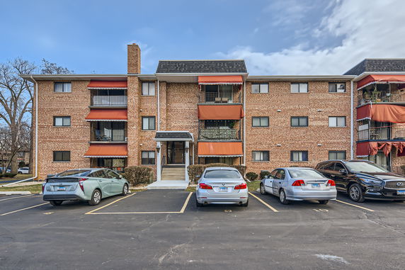 Front view of a three-story brick apartment building with balconies and awnings.