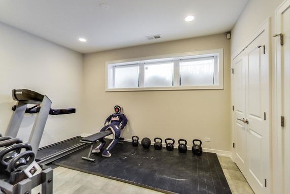 Interior of a home gym with exercise equipment including a treadmill, weight bench, and kettlebells.