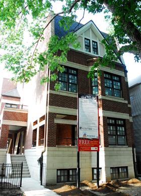 Front view of a multi-story brick house with a peaked roof.