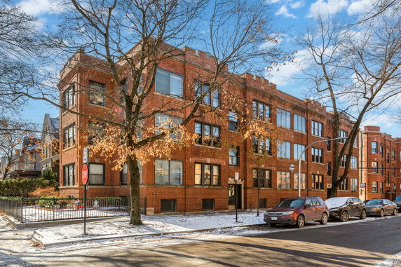 Front view of a three-story brick building with large windows and trees in the foreground.