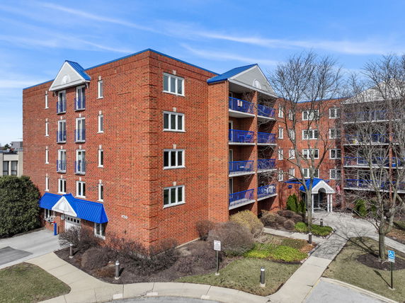 Front view of a multi-story brick apartment building with blue balconies and awnings.