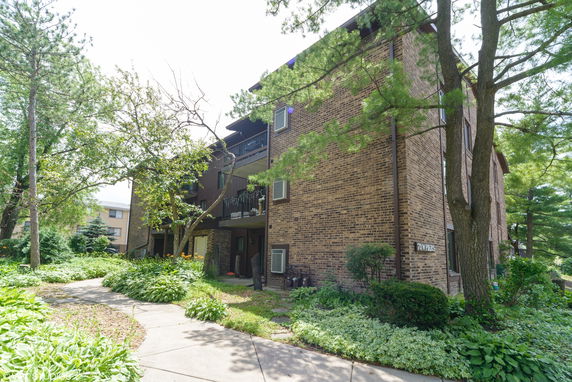 Front view of a multi-story brick building with balconies and surrounding greenery.
