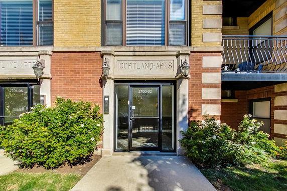 Front view of an apartment building entrance with brick facade and glass doors.