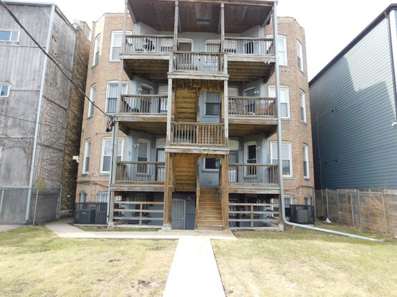 Rear elevation view of a multi-story residential building with wooden balconies.