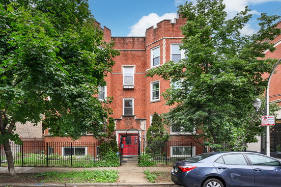Front view of a brick residential building with a red entrance gate and multiple windows.