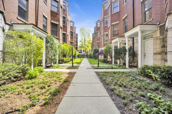 Front view of red brick residential buildings with a central walkway and landscaped gardens.