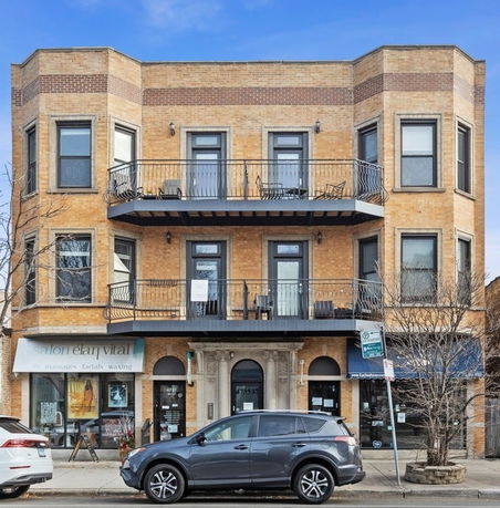Front view of a three-story brick building with balconies on the second and third floors.