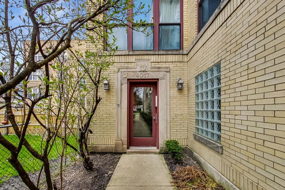 Front view of a brick building entrance with a glass door and surrounding windows.
