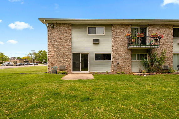 Front view of a two-story brick and siding apartment building with balconies and a grassy lawn.