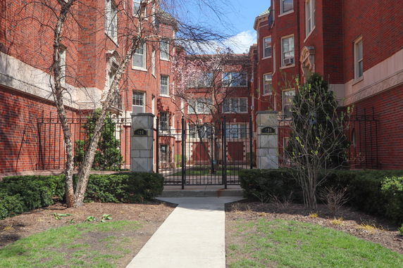 Front view of a multi-story red brick residential building with a gated entrance.
