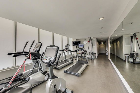 Indoor gym area with exercise machines and mirrors on the walls.