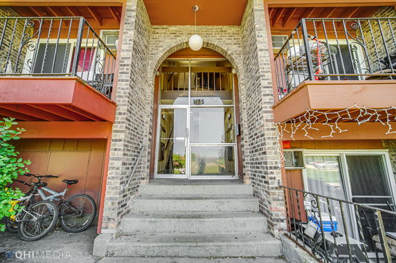 Front view of a brick building with balconies and a central glass entrance.