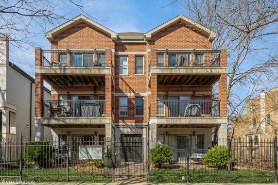 Front view of a multi-story brick building with balconies and a gated entrance.