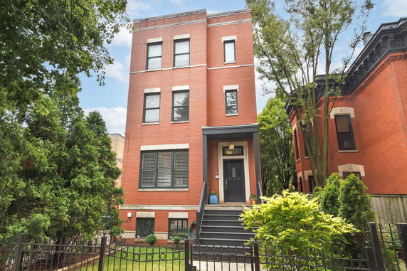 Front view of a three-story brick house with a black door and steps.