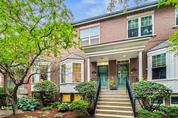 Front view of a two-story brick townhouse with a covered entrance and stairs.
